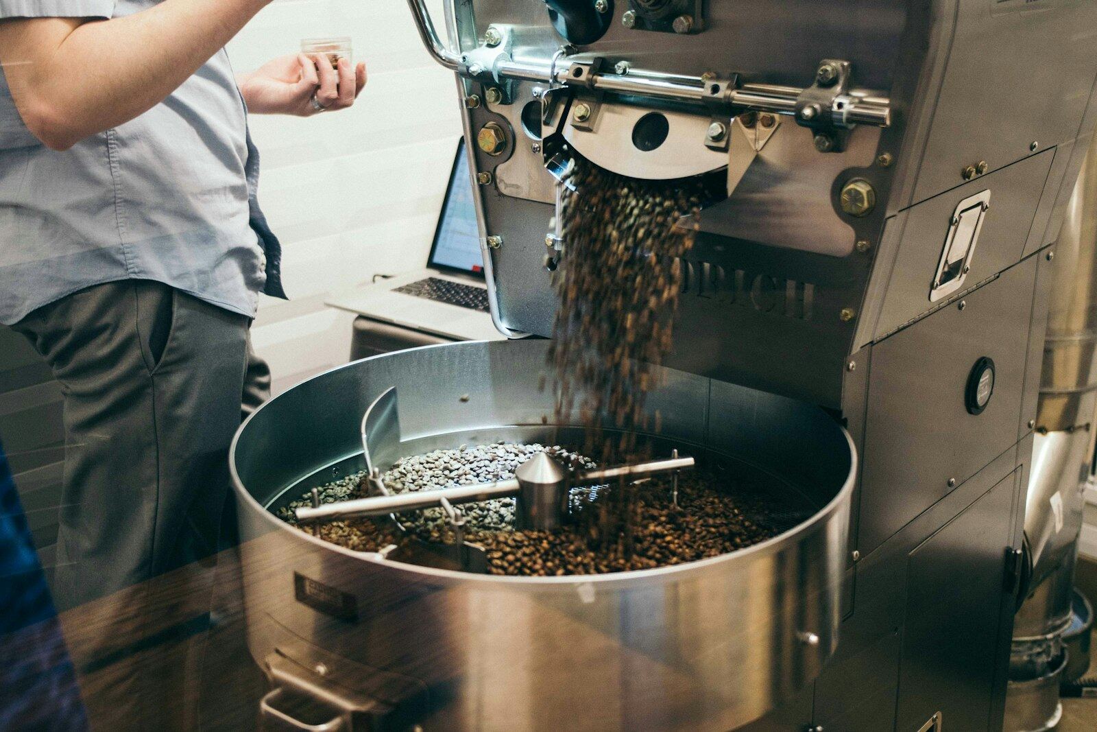 Una tostadora descargando el café recién tostado en la bandeja de enfriado, con un portátil al lado